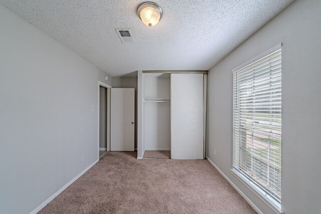 unfurnished bedroom with light carpet, visible vents, multiple windows, and a closet