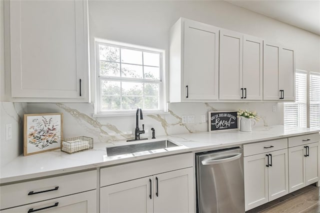 kitchen featuring a sink, light stone counters, backsplash, stainless steel dishwasher, and white cabinetry