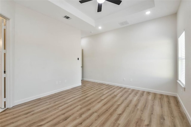 spare room featuring visible vents, light wood-type flooring, recessed lighting, baseboards, and a raised ceiling