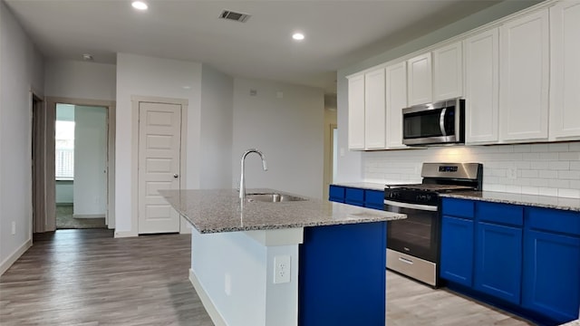 kitchen with visible vents, a center island with sink, a sink, blue cabinetry, and stainless steel appliances