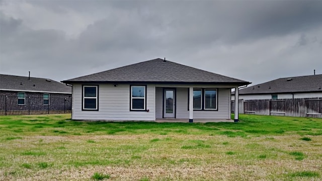 rear view of property with a yard, fence, and a shingled roof