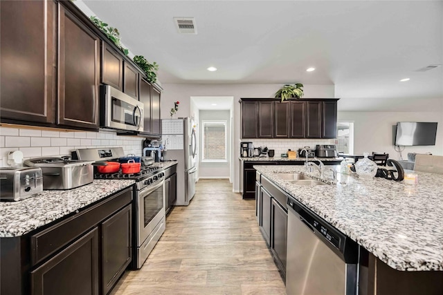 kitchen featuring light stone countertops, visible vents, light wood finished floors, dark brown cabinetry, and appliances with stainless steel finishes