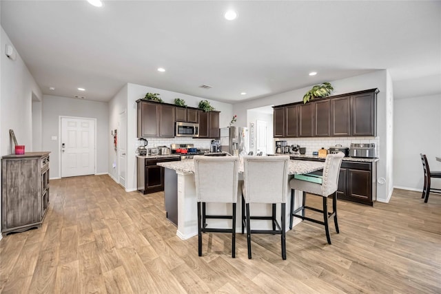 kitchen featuring a center island with sink, light wood-style flooring, dark brown cabinets, appliances with stainless steel finishes, and a kitchen breakfast bar