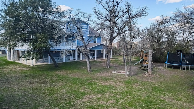 view of yard featuring a playground, a trampoline, a wooden deck, an outdoor fire pit, and a patio area