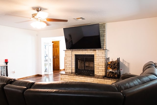 living room featuring visible vents, a brick fireplace, baseboards, wood finished floors, and a ceiling fan