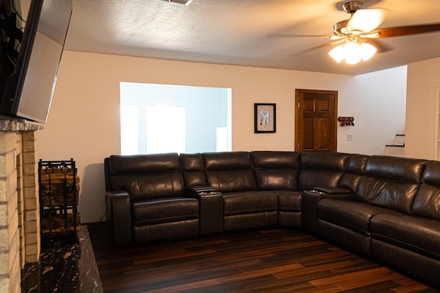 living room featuring a brick fireplace, a textured ceiling, dark wood-type flooring, and ceiling fan