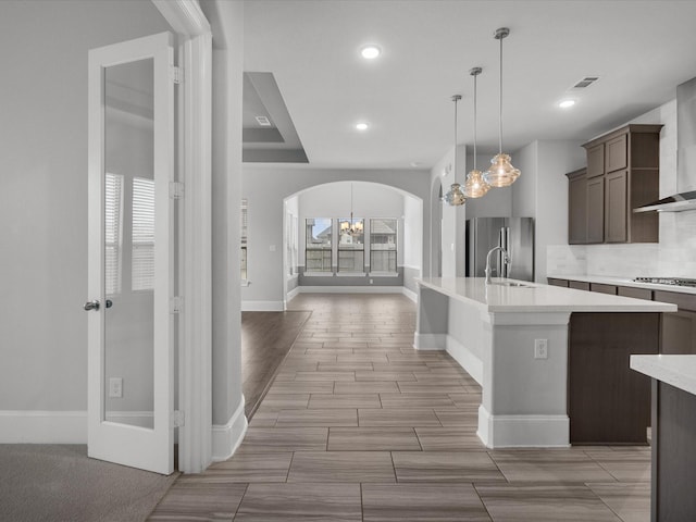 kitchen with arched walkways, a sink, light countertops, appliances with stainless steel finishes, and wall chimney exhaust hood