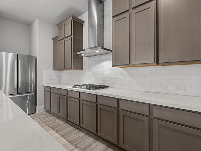 kitchen with decorative backsplash, appliances with stainless steel finishes, wall chimney range hood, and light stone countertops