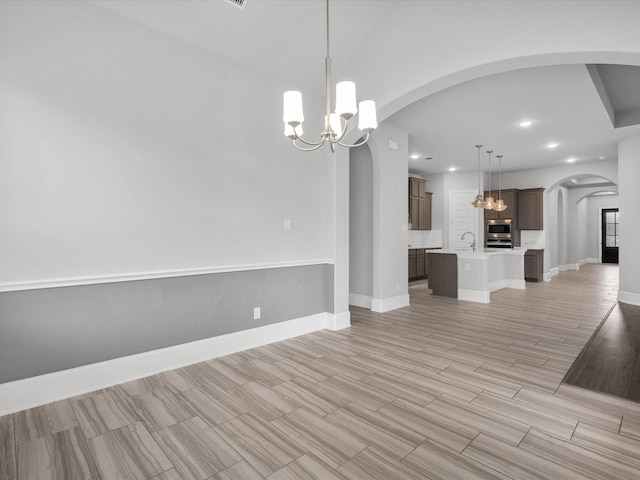 unfurnished dining area featuring baseboards, a chandelier, recessed lighting, arched walkways, and a sink