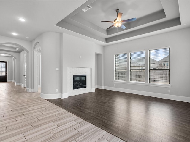 unfurnished living room with a glass covered fireplace, visible vents, a raised ceiling, and wood finished floors