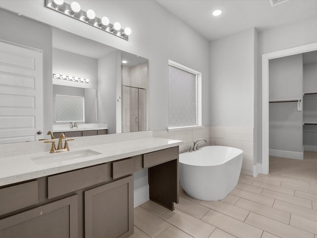 bathroom with visible vents, a walk in closet, a freestanding bath, a stall shower, and vanity