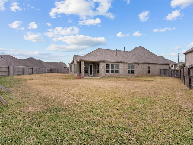 rear view of house with a yard, brick siding, and a fenced backyard