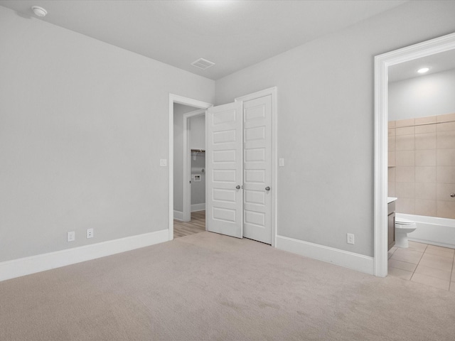 unfurnished bedroom with baseboards, ensuite bathroom, and carpet flooring