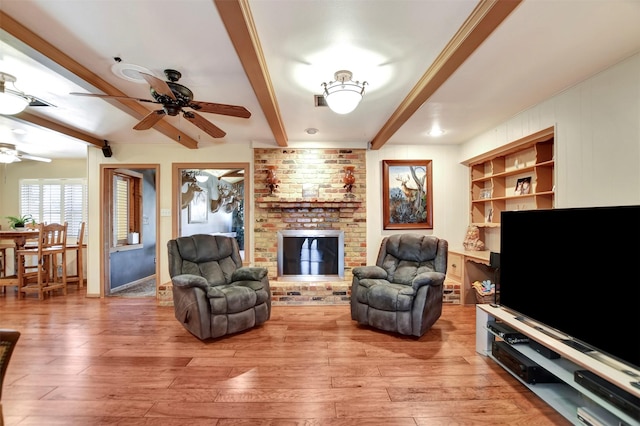 living room featuring beam ceiling, built in shelves, a ceiling fan, light wood finished floors, and a brick fireplace