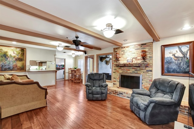 living room featuring beamed ceiling, a brick fireplace, and wood finished floors