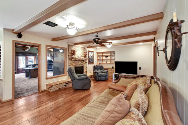 living room with visible vents, a brick fireplace, beam ceiling, light wood-style floors, and a ceiling fan