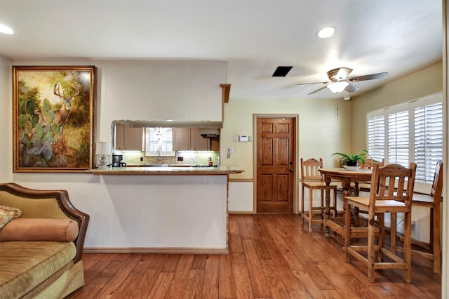 kitchen with backsplash, ceiling fan, light countertops, a peninsula, and wood finished floors