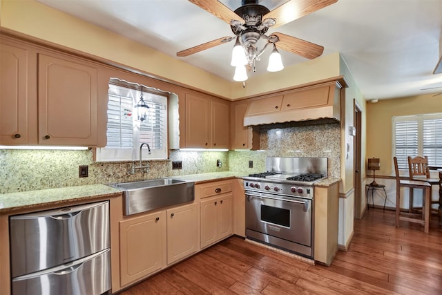 kitchen with wood finished floors, custom exhaust hood, a sink, decorative backsplash, and appliances with stainless steel finishes