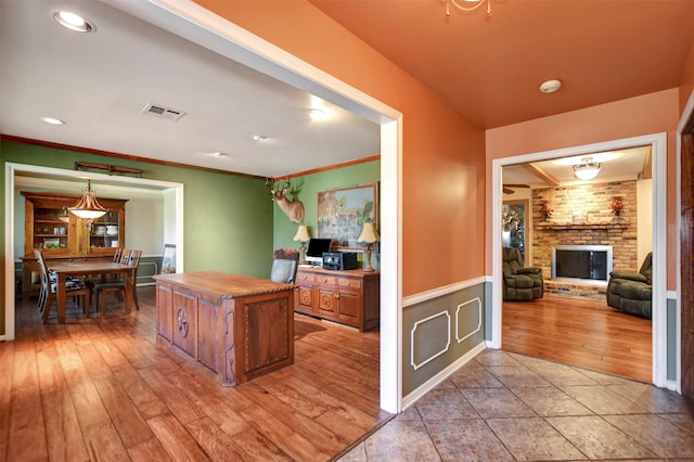 kitchen featuring visible vents, light wood finished floors, a kitchen island, a fireplace, and crown molding