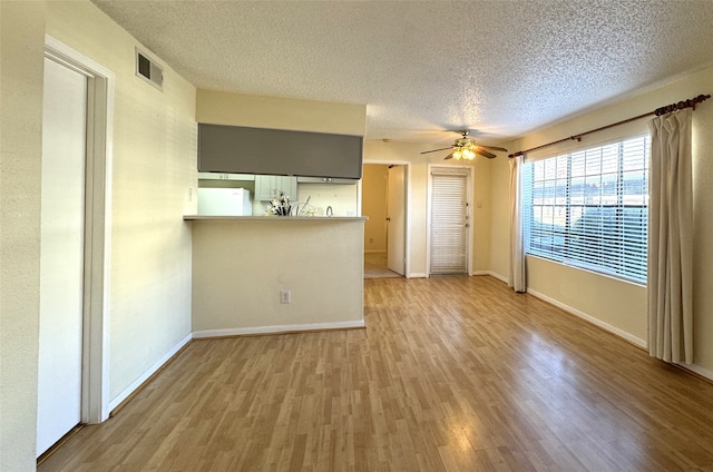 unfurnished living room featuring visible vents, baseboards, light wood-style flooring, a textured ceiling, and a ceiling fan