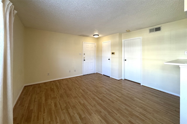 empty room with visible vents, baseboards, a textured ceiling, and wood finished floors