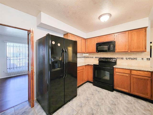 kitchen with light stone countertops, backsplash, black appliances, and brown cabinets