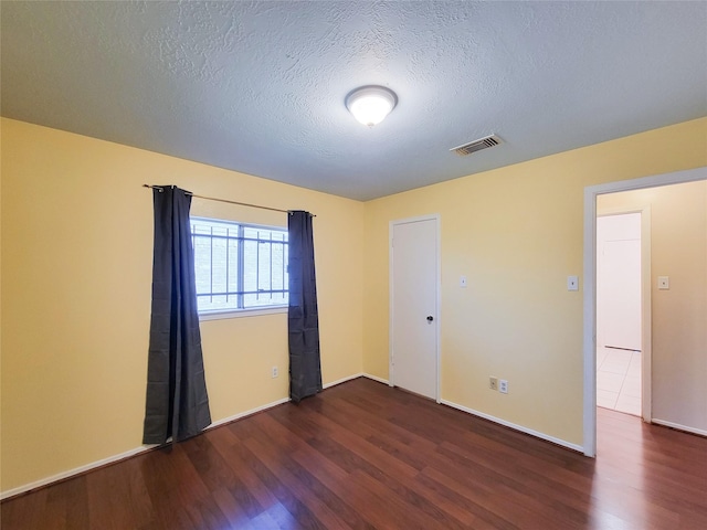 unfurnished room featuring visible vents, a textured ceiling, baseboards, and wood finished floors