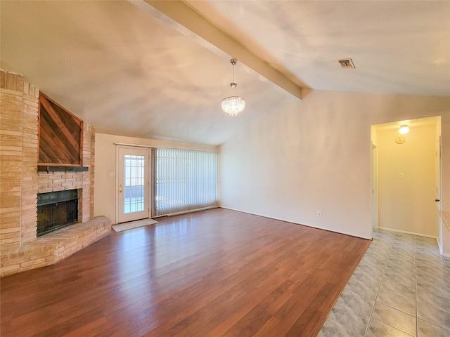 unfurnished living room with visible vents, a fireplace, lofted ceiling with beams, and wood finished floors