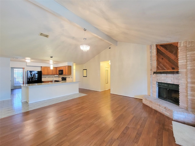 unfurnished living room featuring visible vents, light wood-style floors, a brick fireplace, and vaulted ceiling with beams