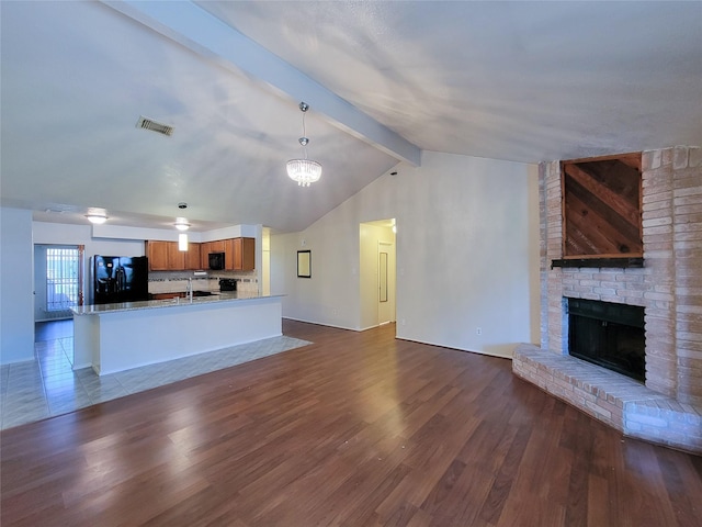 unfurnished living room featuring visible vents, dark wood-style flooring, a sink, a brick fireplace, and vaulted ceiling with beams