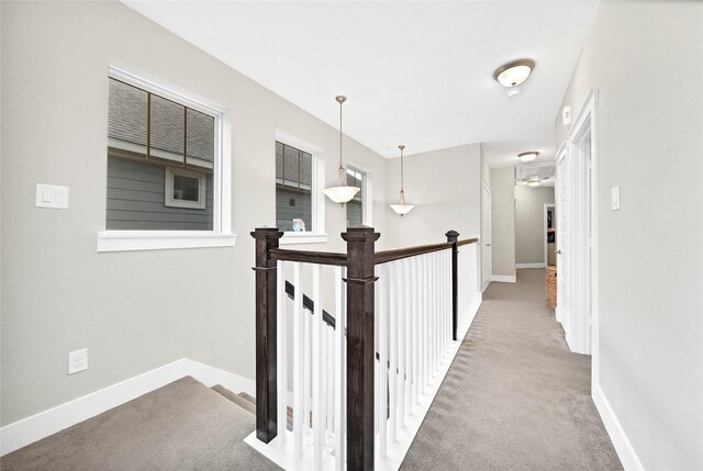 hallway with an upstairs landing, baseboards, and carpet floors