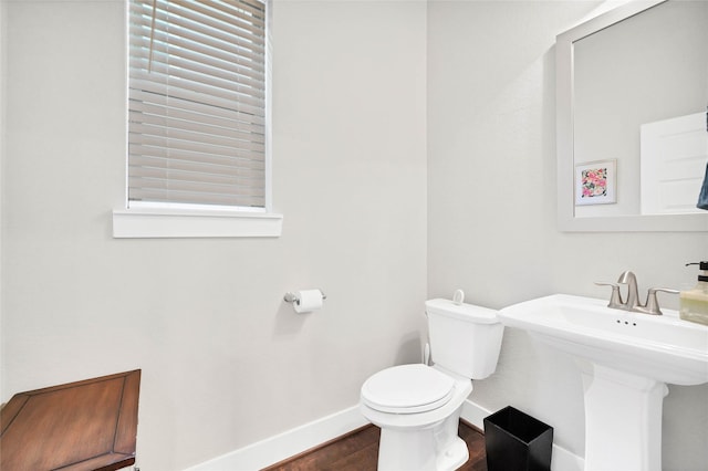 half bath featuring a sink, baseboards, toilet, and wood finished floors