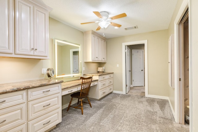 office featuring a ceiling fan, a textured ceiling, built in desk, baseboards, and light colored carpet