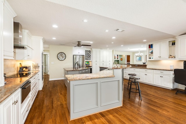 kitchen with wall chimney range hood, dark wood-style floors, stainless steel refrigerator with ice dispenser, a large island, and black electric cooktop