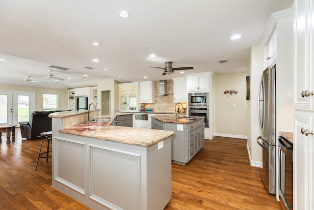 kitchen featuring a large island, a sink, stainless steel appliances, wall chimney range hood, and decorative backsplash