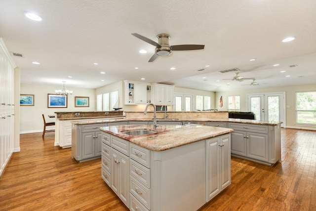 kitchen with visible vents, a peninsula, light wood-style flooring, an island with sink, and a sink