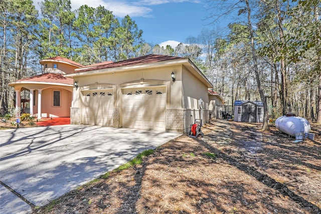 view of property exterior with brick siding, a shed, concrete driveway, stucco siding, and a garage