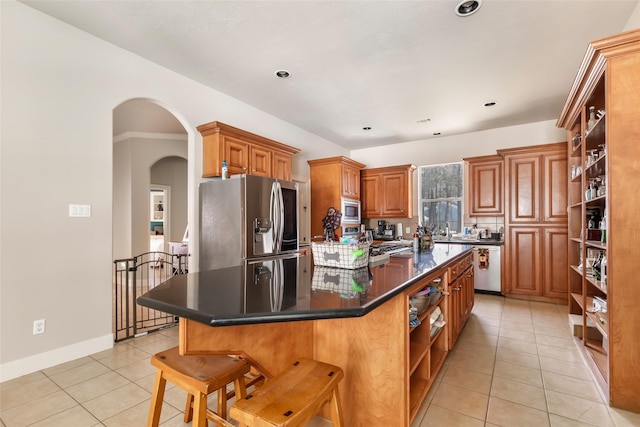 kitchen featuring open shelves, dark countertops, a center island, stainless steel appliances, and brown cabinetry