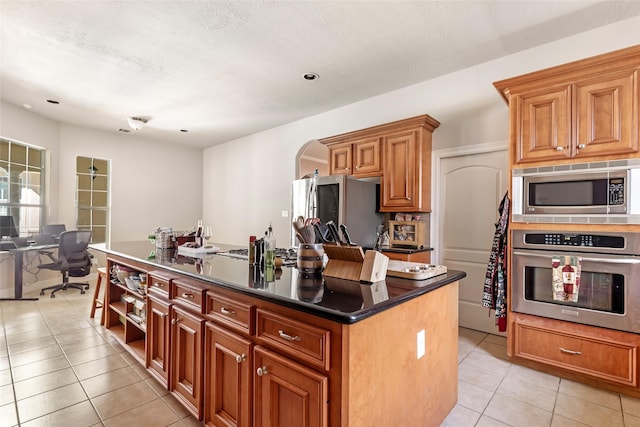 kitchen featuring light tile patterned floors, a kitchen island, arched walkways, stainless steel appliances, and dark countertops