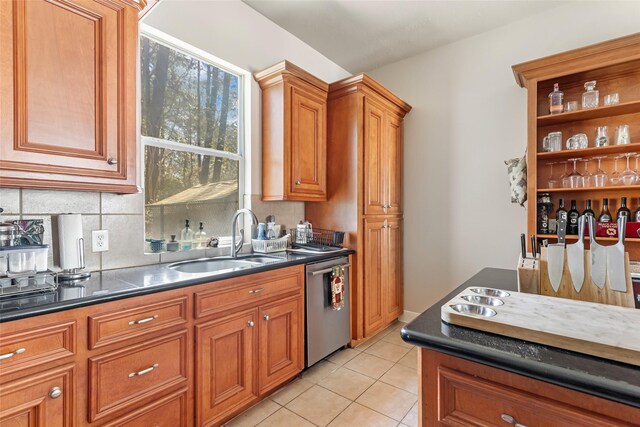 kitchen featuring stainless steel dishwasher, dark countertops, brown cabinetry, and a sink