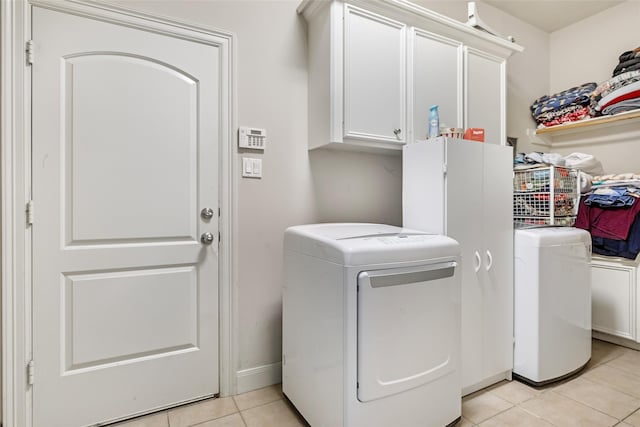 clothes washing area featuring light tile patterned flooring, washing machine and dryer, and cabinet space