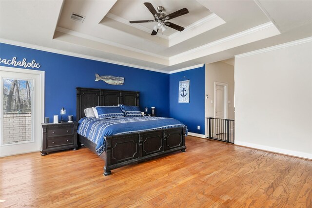 bedroom with baseboards, visible vents, light wood finished floors, ornamental molding, and a raised ceiling