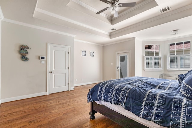 bedroom featuring a tray ceiling, visible vents, wood finished floors, and ornamental molding