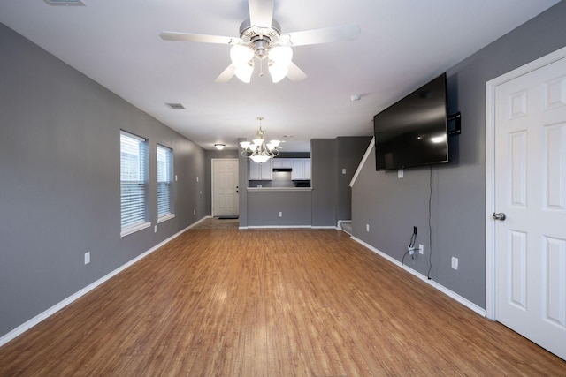 unfurnished living room with ceiling fan with notable chandelier, wood finished floors, visible vents, and baseboards