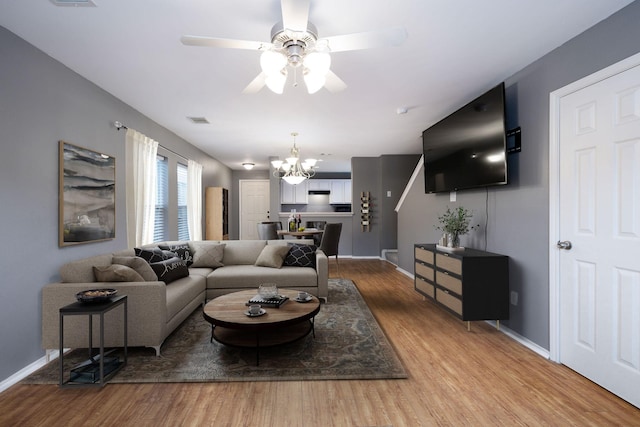 living room with visible vents, ceiling fan with notable chandelier, baseboards, and wood finished floors