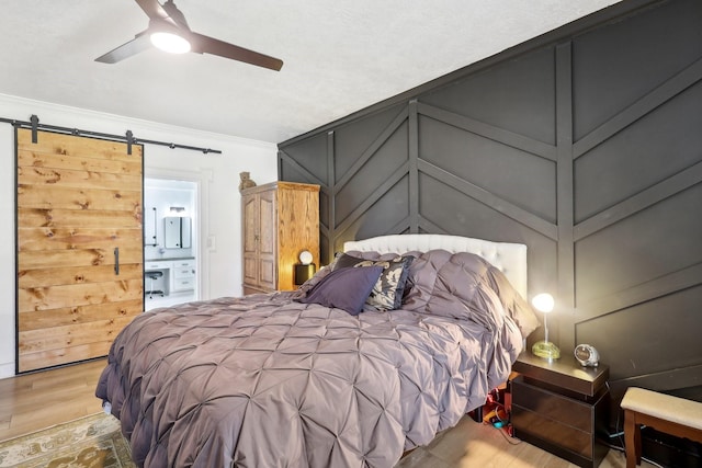 bedroom with wood finished floors, ornamental molding, ensuite bathroom, a barn door, and a decorative wall