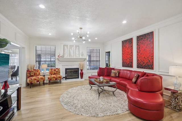 living area with crown molding, a glass covered fireplace, wood finished floors, a decorative wall, and a textured ceiling