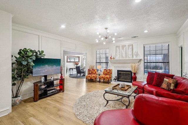 living room with a chandelier, plenty of natural light, ornamental molding, wood finished floors, and a decorative wall