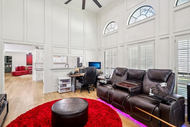 interior space featuring light wood finished floors, a high ceiling, a ceiling fan, and a decorative wall