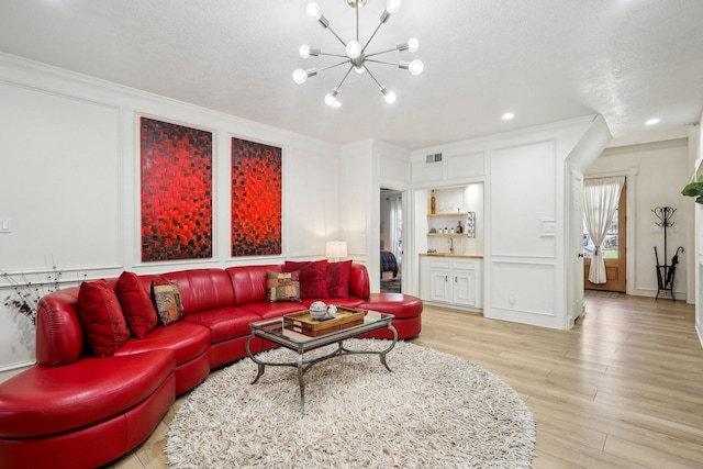 living room with a decorative wall, visible vents, an inviting chandelier, and light wood-style floors